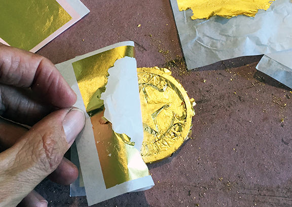 Applying patent gold leaf to a ceremonial brass coin